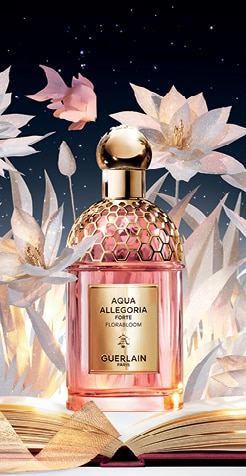Guerlain Aqua Allegoria Forte Florabloom parfüm arany kupakkal és rózsaszín üvegben, papírvirág dekorációval csillagos háttér előtt.